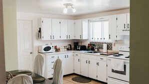 Une cuisine moderne avec des meubles blancs, un four à micro-ondes, une machine à café et une cuisinière.