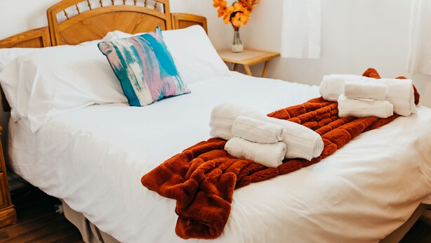 Un lit bien fait, avec des draps blancs, un coussin coloré et une couverture rouge.