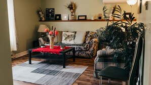 Un salon avec un canapé, une table basse et un fauteuil. On y trouve une étagère avec des objets décoratifs et une plante.