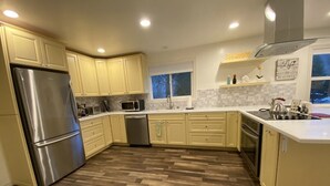 Moderni keittiö, jossa on vaaleankeltaiset kaapit, ruostumattomasta teräksestä valmistettu jääkaappi ja kalanruotokuviollinen puulattia.