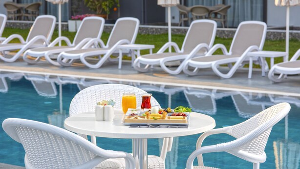 A poolside dining area with white wicker chairs and a table set with breakfast. - A Suite Side (Manavgat)