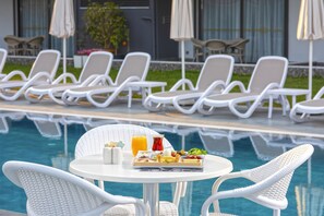 A poolside dining area with white wicker chairs and a table set with breakfast.