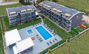 A modern hotel with multiple balconies, a swimming pool, and a covered outdoor seating area.