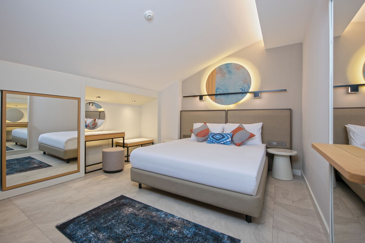 A modern bedroom with a large bed, bedside tables, a mirror, and a round wall light.