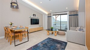 A modern living room with a dining area, a sofa, a TV, and a view of a balcony with a jacuzzi. - A Suite Side (Manavgat)