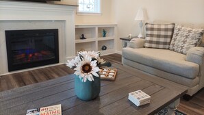 Ein Wohnzimmer mit Kamin, einer Couch, einem Couchtisch mit Blumenvase und einem Fernseher.