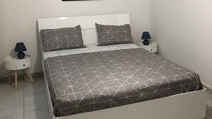 A bedroom with a white bed, two nightstands, a lamp on each, and a painting on the wall. - Magnificent apartment 2 km from the beach (Le Gosier)
