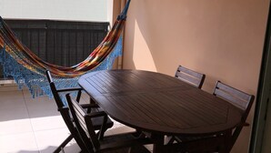 A dining area with a wooden table and chairs, a hammock, and a view of buildings in the background. - Magnificent apartment 2 km from the beach (Le Gosier)
