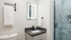 Un baño moderno con inodoro, lavabo, espejo y cabina de ducha de vidrio.