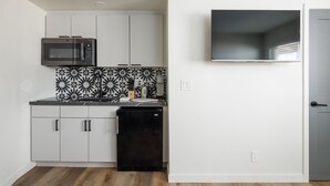 Cocina compacta con armarios blancos, refrigerador negro, microondas y un salpicadero con diseño.