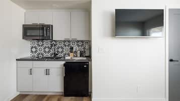 A compact kitchen with white cabinets, a black refrigerator, a microwave, and a patterned backsplash.