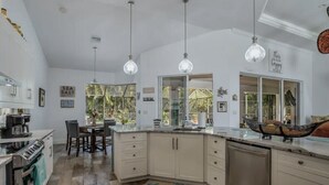 A modern kitchen with white cabinets, a central island, pendant lights, and a view of the outdoors.