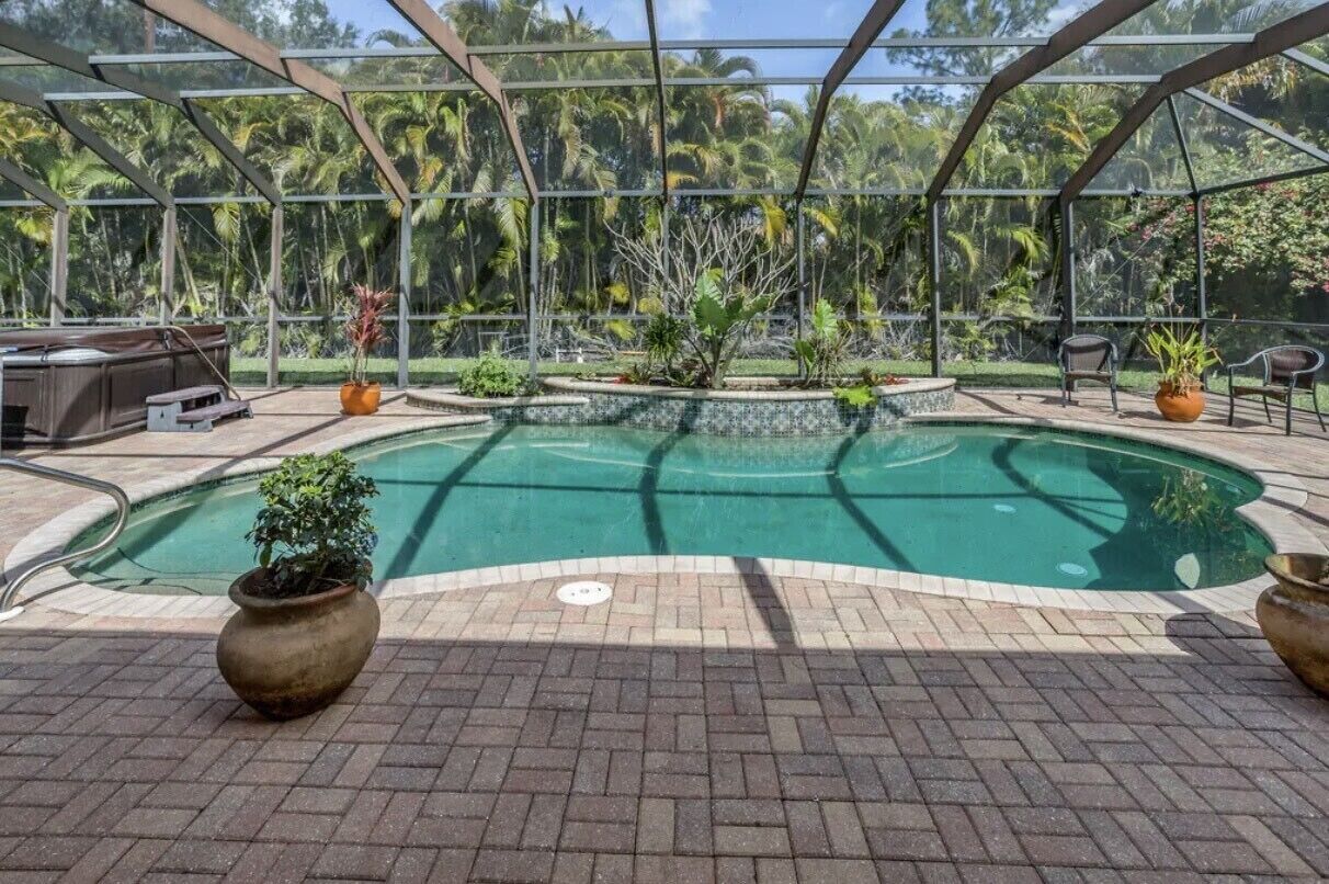 Un espace piscine intérieure doté d’un toit en verre, entouré de plantes tropicales et recouvert d’un sol en briques.