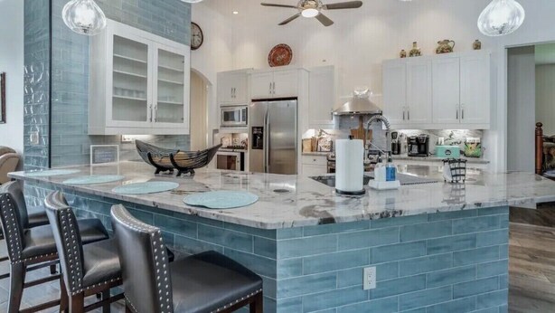 A modern kitchen with a marble island, white cabinets, and a ceiling fan.