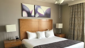 A hotel room with a large bed, two bedside tables, a nightstand, a wall-mounted lamp, and abstract wall art. - Wyndham Ocean Walk 2BR (Daytona Beach)