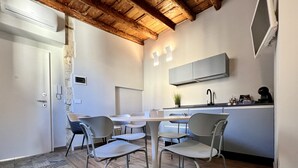 A modern kitchen with a dining area, featuring a wooden ceiling, white cabinetry, and a patterned rug. - Suite Amalfitania, Ortigia, Syracuse. (Siracusa)