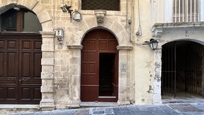 A historic building with a central arched doorway, a large wooden door, and a stone facade. - Suite Amalfitania, Ortigia, Syracuse. (Siracusa)