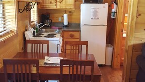 Cozinha compacta com armários de madeira, micro-ondas, geladeira e mesa de jantar com cadeiras.