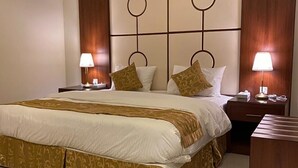 A hotel room with a large bed, two bedside tables with lamps, a wooden headboard with circular designs, and a wooden nightstand. - Rihanna Inn APT - Riyadh (Riyadh)