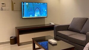 A modern living room with a flat-screen TV mounted on the wall, a dark wooden coffee table, and a grey sofa. - Rihanna Inn APT - Riyadh (Riyadh)