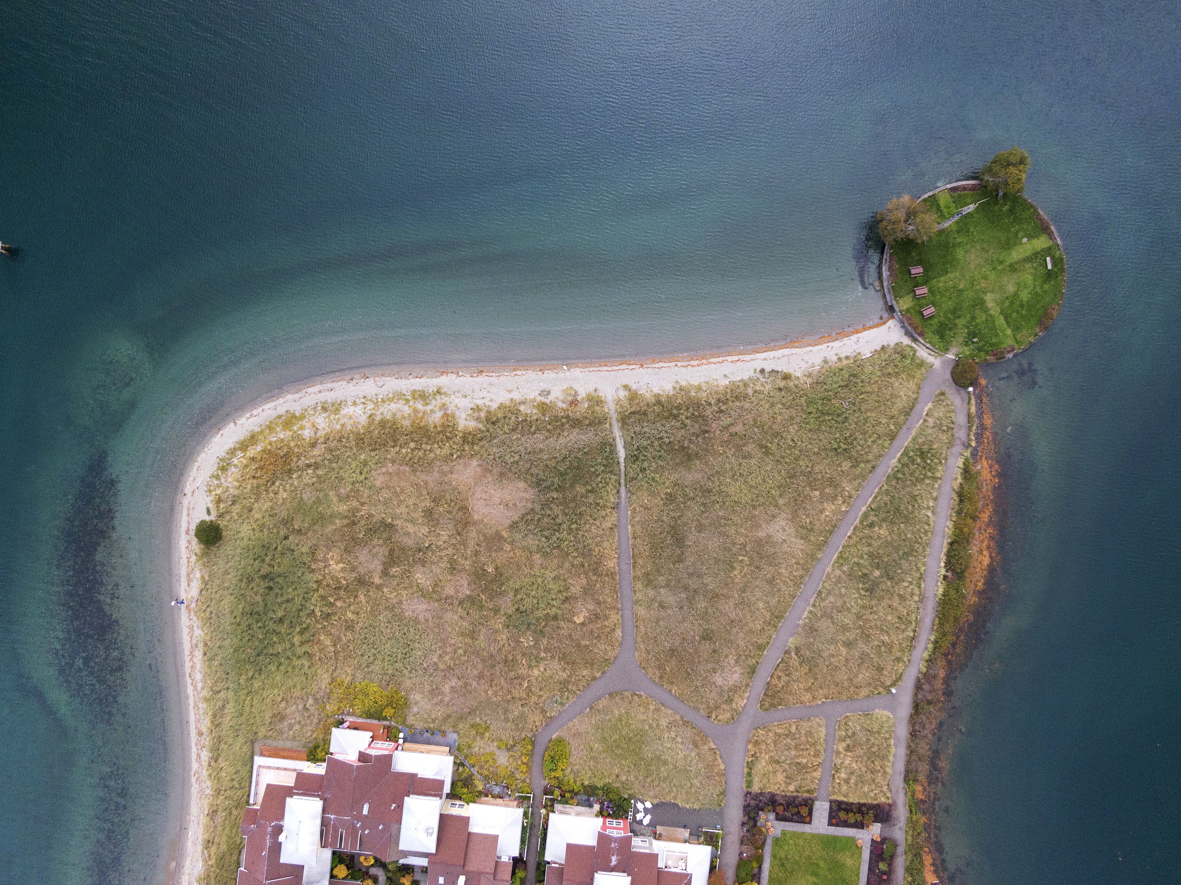 Eine Luftaufnahme eines Küsteneigentums mit Strand, einem kleinen Park und einer Straße, die zu einer Ansammlung von Gebäuden führt.