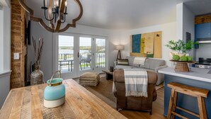 A modern living room with a wooden dining table, a sofa, and a kitchen area with a blue countertop. - Fish Creek Beach House, Westview: 2 Bed, 2 Bath (Fish Creek)