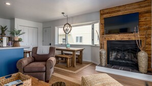 A living room with a fireplace, a television mounted on a wooden wall, a brown leather chair, and a wooden coffee table. - Fish Creek Beach House, Westview: 2 Bed, 2 Bath (Fish Creek)