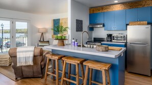 A modern kitchen with blue cabinets, a stainless steel refrigerator, a microwave, and a sink. There are wooden stools and a plant on the counter. - Fish Creek Beach House, Westview: 2 Bed, 2 Bath (Fish Creek)