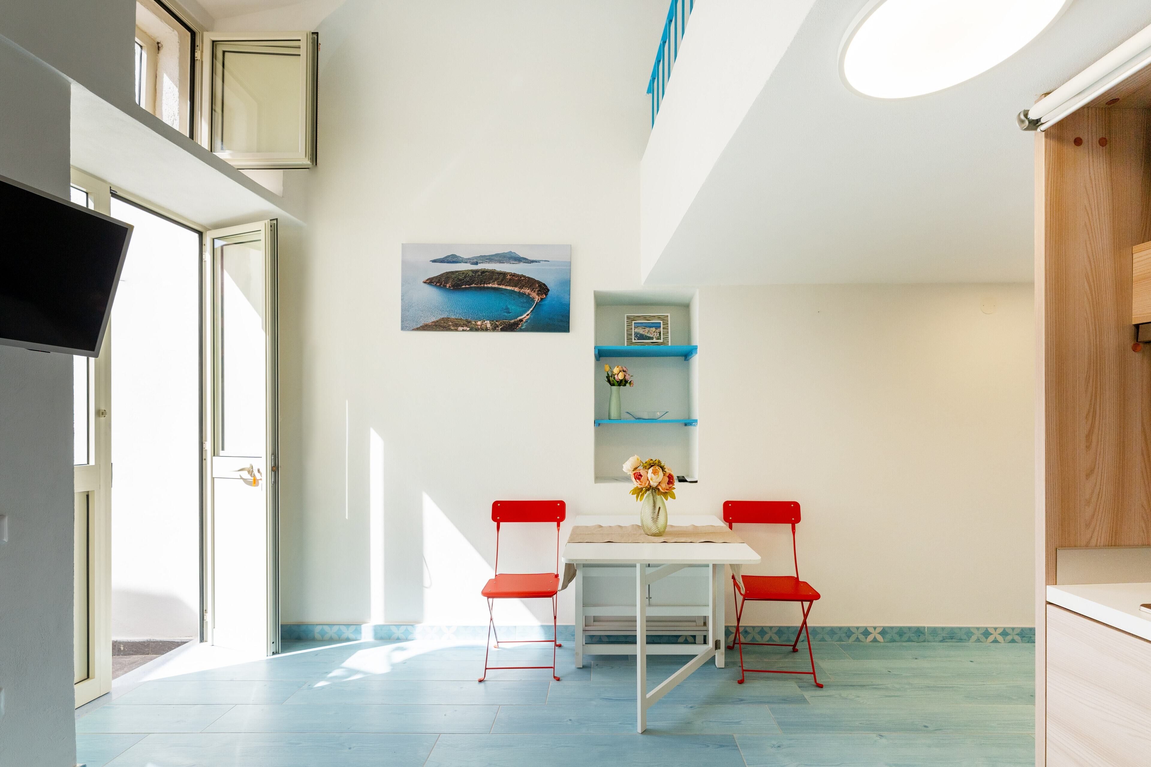 A dining area with a table, chairs, and a painting of a coastal scene.