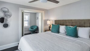 Een slaapkamer met een groot bed, een plafondventilator, een stoel en een nachtkastje met een lamp.