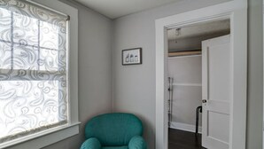 Een kamer met een blauwgroene stoel, een raam met gordijnen met patroon, en een deur naar een inloopkast.