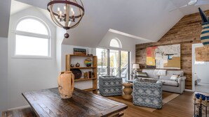 A spacious loft with a high ceiling, wooden beams, a dining area with a rustic table, a cozy seating area with patterned cushions, and a large window providing natural light. - Fish Creek Beach House, Grandview Condo: Entire Top Floor - 4 Bed, 2 Bath (Fish Creek)