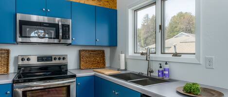 Una cocina moderna con armarios azules, electrodomésticos de acero inoxidable, un ventanal con vistas y un escurreplatos.