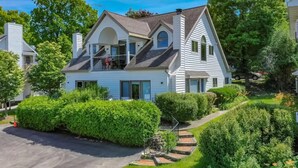 A two-story house with a balcony, surrounded by well-maintained hedges and a driveway. - Fish Creek Beach House, Grandview Condo: Entire Top Floor - 4 Bed, 2 Bath (Fish Creek)