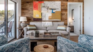 A modern living room with a large abstract painting, a sofa, a coffee table, and a view through a glass door. - Fish Creek Beach House, Grandview Condo: Entire Top Floor - 4 Bed, 2 Bath (Fish Creek)