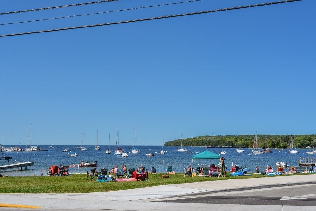 Un port de plaisance avec des bateaux, des gens se détendant sur l’herbe et un ciel bleu dégagé.