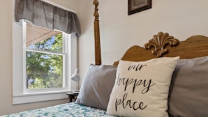 A bedroom with a bed, a window with a view of trees, a bedside table with a lamp, and a decorative headboard.