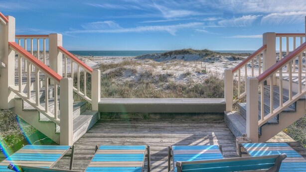 A wooden deck with a view of a beach and dunes.