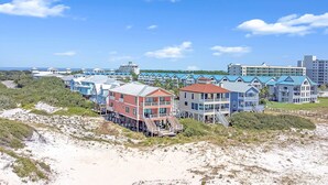 A coastal hotel with multiple-story buildings, some with balconies, situated on a sandy beach with a clear blue sky.