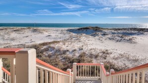 A beach view from a balcony with a railing, sandy dunes, and the ocean.
