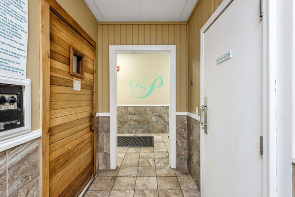 Un pasillo con pared de madera, piso de baldosas de piedra, puerta de cristal con un logotipo y un cartel que indica un baño de vapor.