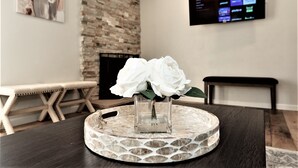 A living room with a stone fireplace, a flat-screen TV mounted on the wall, and a round table with a vase of white flowers. - Updated home in safe, quiet neighborhood with lots of amenities! (San Diego)