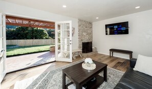 Een moderne woonkamer met een open haard, een aan de muur bevestigde televisie en een grote schuifpui naar een achtertuin.