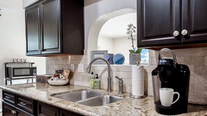 A modern kitchen with dark cabinets, a granite countertop, a sink, a coffee maker, and a microwave. - Updated home in safe, quiet neighborhood with lots of amenities! (San Diego)