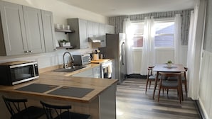 A modern kitchen with grey cabinets, a microwave, a toaster, and a dining area with a table and chairs. - Brand new Apt B: 1 Bedroom 1 Bath in the Heart of Downtown Ellsworth (Ellsworth)