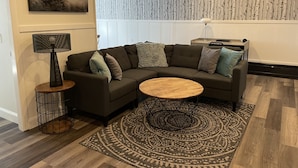A modern living room with a sectional sofa, a round coffee table, a patterned rug, a floor lamp, and a wall-mounted air conditioner. - Brand new Apt B: 1 Bedroom 1 Bath in the Heart of Downtown Ellsworth (Ellsworth)