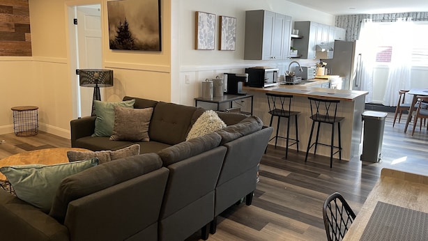 A modern living room with a grey sofa, a coffee table, and a dining area with a bar stool. - Brand new Apt B: 1 Bedroom 1 Bath in the Heart of Downtown Ellsworth (Ellsworth)