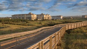 A wooden boardwalk leading to a multi-story building with a flat roof, surrounded by grassy areas and trees. - Long Beach WA  Oceanfront 4th of July week (Long Beach)