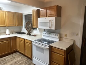 A kitchen with wooden cabinets, a white stove, a microwave, and a window with blinds. - Corporate Housing (Cedar Hill)