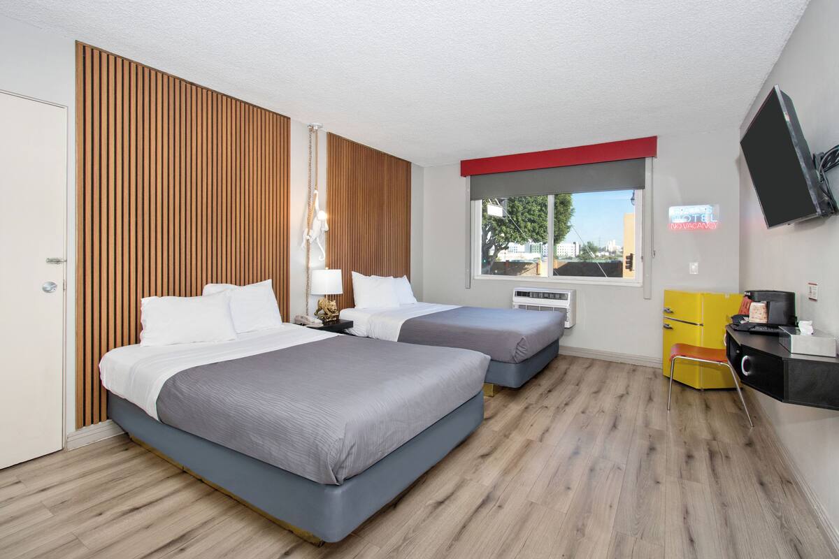Una habitación de hotel con dos camas, un televisor, un escritorio, una silla, una ventana y una puerta.